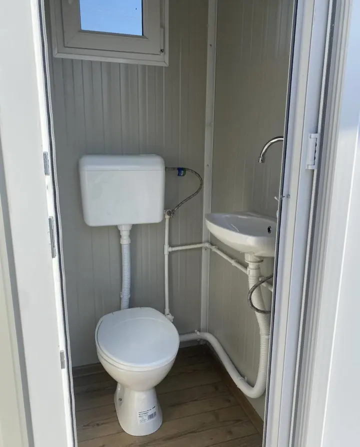 Flushing toilet with tank and wall sink inside a portable restroom cabin