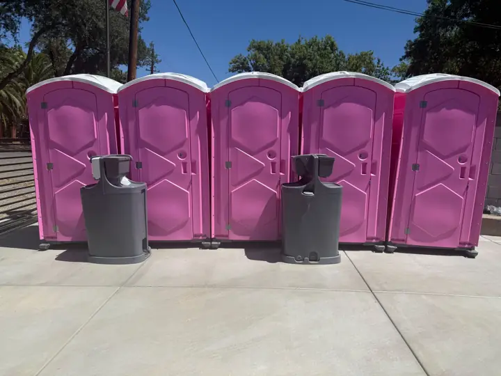 Row of five pink porta potties with two handwashing stations on pavement