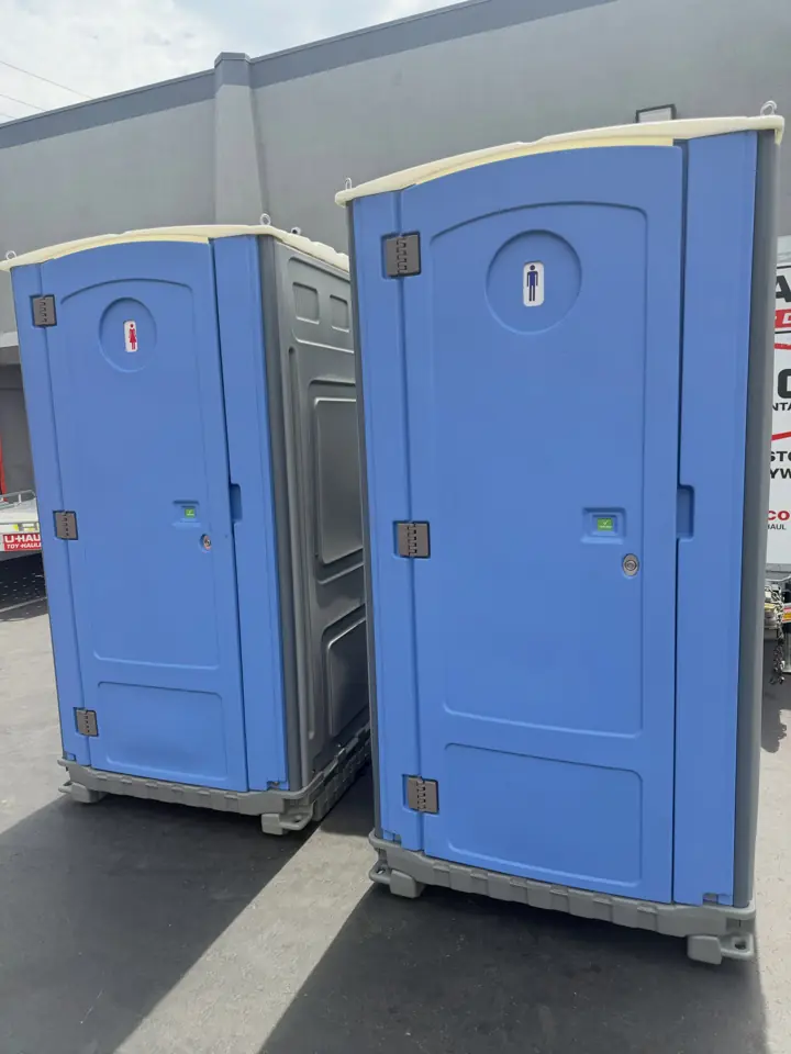 Two blue standard porta potties in a paved lot